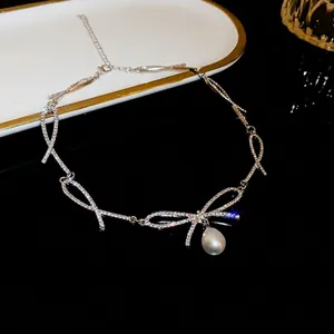 Elegant rhinestone bow necklace with pearl pendant on a black reflective surface