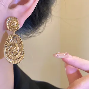 Close-up of stylish gold textured oval drop earrings worn on an Asian female model's ear