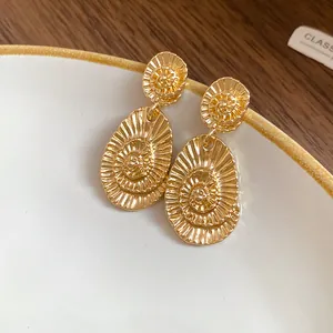 Macro view of gold oval stud earrings featuring elegant spiral texture on white plate.