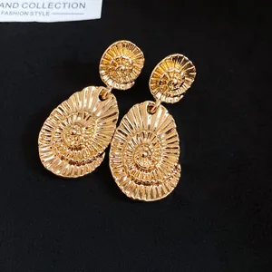 Close-up of golden oval earrings with intricate spiral texture on black background