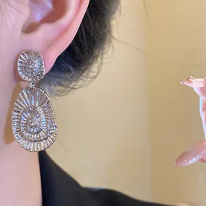 Close-up view of silver oval drop earrings with spiral radial texture worn on an earlobe