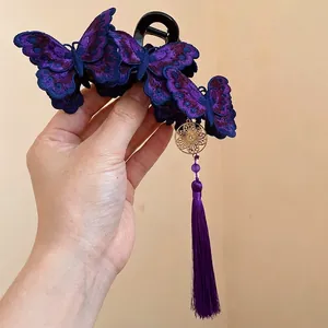 Hand holding a purple embroidered butterfly hair claw clip featuring a long purple silk tassel