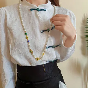 Primo piano di una lunga collana di perle con ciondoli placcati in oro su un qipao