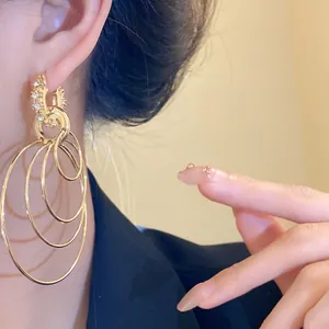 Close-up of golden multi-layered hoop earrings with rhinestone details worn by a model