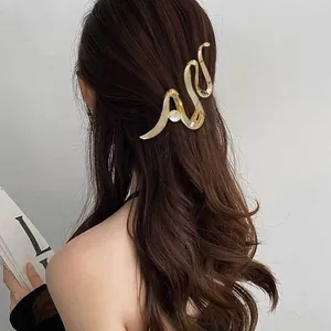 Detail shot of a minimalist gold geometric hair claw clip with pearl on long wavy hair.