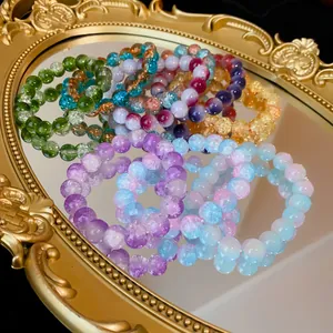 Vista dettagliata di braccialetti elastici con perle di vetro crackle sfumate su specchio.