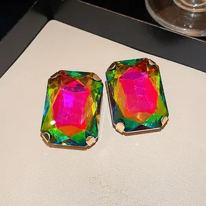 Close-up detail of large iridescent rectangular stud earrings with gold-tone claw setting.