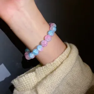 Primo piano di perle in vetro craquelé rosa e blu su un braccialetto elastico al polso