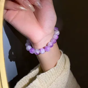 Dettaglio di un braccialetto elastico con perle in vetro craquelé viola su un polso.