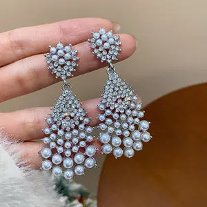 Close-up detail of silver-toned dangle earrings with pearls and shimmering rhinestones ornament.