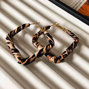 Detail of leopard print leather-wrapped square hoop earrings on a white surface.