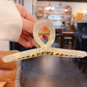 Gros plan d'une pince à cheveux en acétate blanc irisé tenue à la main dans un café