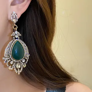 Détail de boucles d'oreilles de style cour vintage avec pierre goutte verte et strass