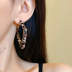 Detail view of a stylish leopard print leather wrapped geometric hoop earring worn by a model