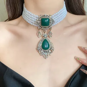 Détail d'un collier ras de cou en perles vintage avec pendentifs goutte vert émeraude.