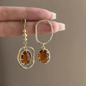 Vintage asymmetric gold earrings featuring amber zircon stones, handheld elegant display