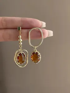 Detail showing asymmetric amber zircon earrings with gold-tone metal hoops and beads.