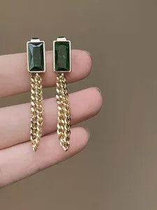 Close-up of vintage gold earrings with emerald green zircon and dangling chain details