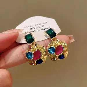 Close-up detail of vintage gold-tone earrings with vibrant multi-color resin inlays.