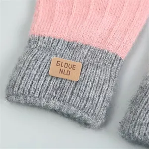 Close-up of pink and grey knitted gloves with a leather GLOVE NLD tag