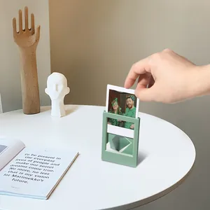 Hand legt ein Foto in einen Morandi-grünen 3-Zoll-Mini-Polaroidrahmen auf den Tisch.
