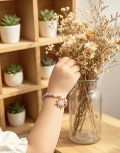 Child wearing an evil eye beaded bracelet with gold sun charm near dried flowers.