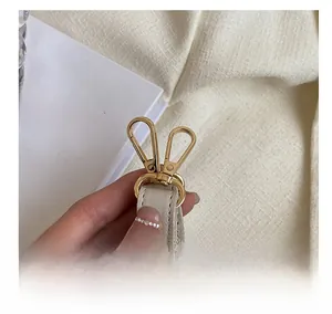 Detailed view of polished gold-tone metal hardware hooks on textured beige bag strap
