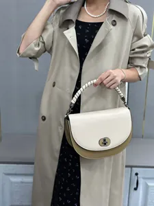 Two-tone saddle bag with metallic lock shown on model wearing a trench coat