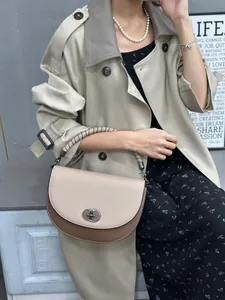 Fashionable color-block saddle bag with lock closure, shown in a lifestyle setting.
