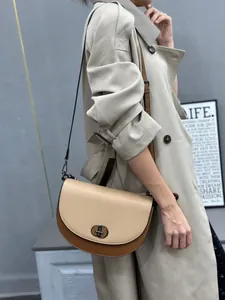 Stylish color-blocked saddle bag with metal lock worn by a model in a trench coat