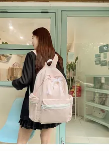 Pink student backpack with lace bow detail shown on model in cafe