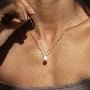 Elegant minimalist opal pendant necklace with a delicate gold chain worn by a female model.