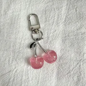 Close-up of glittery pink resin cherry keychain with silver metallic clip and leaf