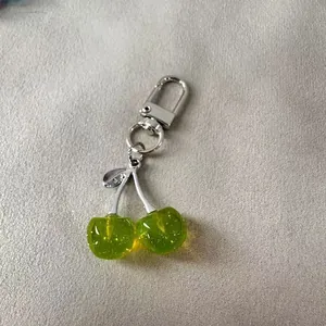 Detailed view of a translucent green cherry charm keychain with glitter and silver metal clasp