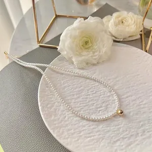 Close-up shot of a delicate white freshwater pearl necklace featuring a single gold bead pendant