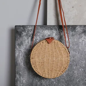 Détail de face d'un sac à bandoulière rond en paille tissée avec lanières brunes