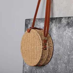 Vue détaillée d'un sac de plage rond en paille tissée avec des lanières en cuir.