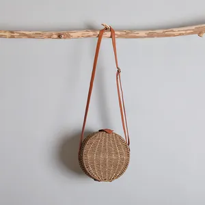 Détail d'un sac à bandoulière rond en paille tissée avec une lanière en cuir brun réglable