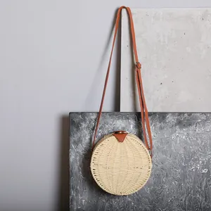 Détail d'un sac rond en paille tressée avec bandoulière en cuir marron et fond gris