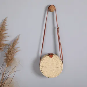 Vue détaillée d'un sac bandoulière rond en paille tissé main suspendu à un crochet mural.