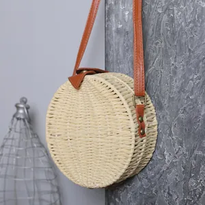 Vue détaillée d'un sac rond en paille tressée avec bandoulière en cuir PU marron élégant