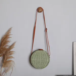Vue détaillée d'un sac bandoulière rond en paille tressée verte avec bandoulière marron.