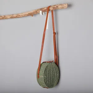 Sac à bandoulière rond en paille tressée verte rétro suspendu à une branche de bois naturel.