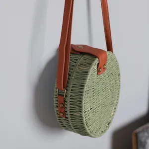Détail de profil d'un sac à bandoulière rond en paille vert sauge avec lanière marron