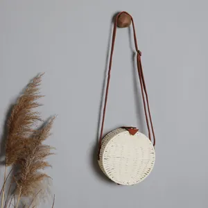 Gros plan d'un sac à bandoulière rond en paille tressée avec bandoulière en cuir brun