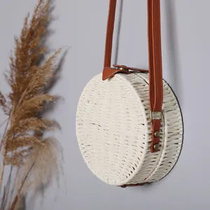 Détail d'un sac à bandoulière rond en paille blanche avec une lanière en simili cuir brun