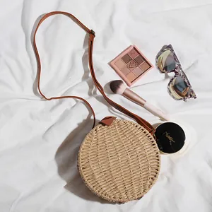 Vue détaillée du sac en paille tressée ronde avec cosmétiques sur fond blanc.