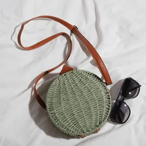 Gros plan d'un sac rond en paille tressée verte avec bandoulière en cuir brun