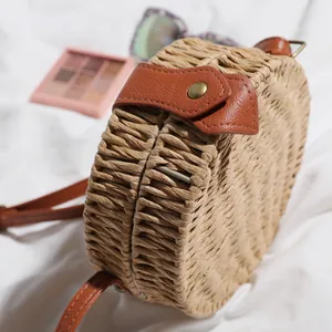 Détail d'un sac de plage rond en paille tressée avec des finitions en cuir marron et bouton.