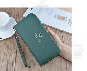 Detail view of a green pebbled leather long wallet with a gold deer logo